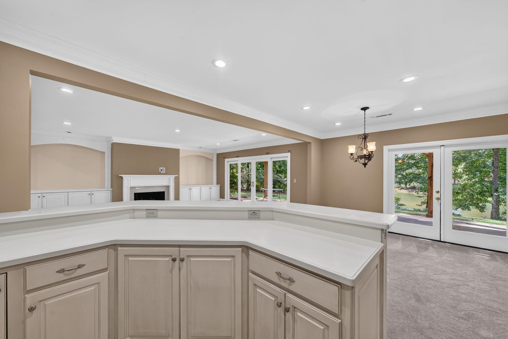 Built-in counter and cabinetry overlook a living area with a fireplace and French doors facing a pond.