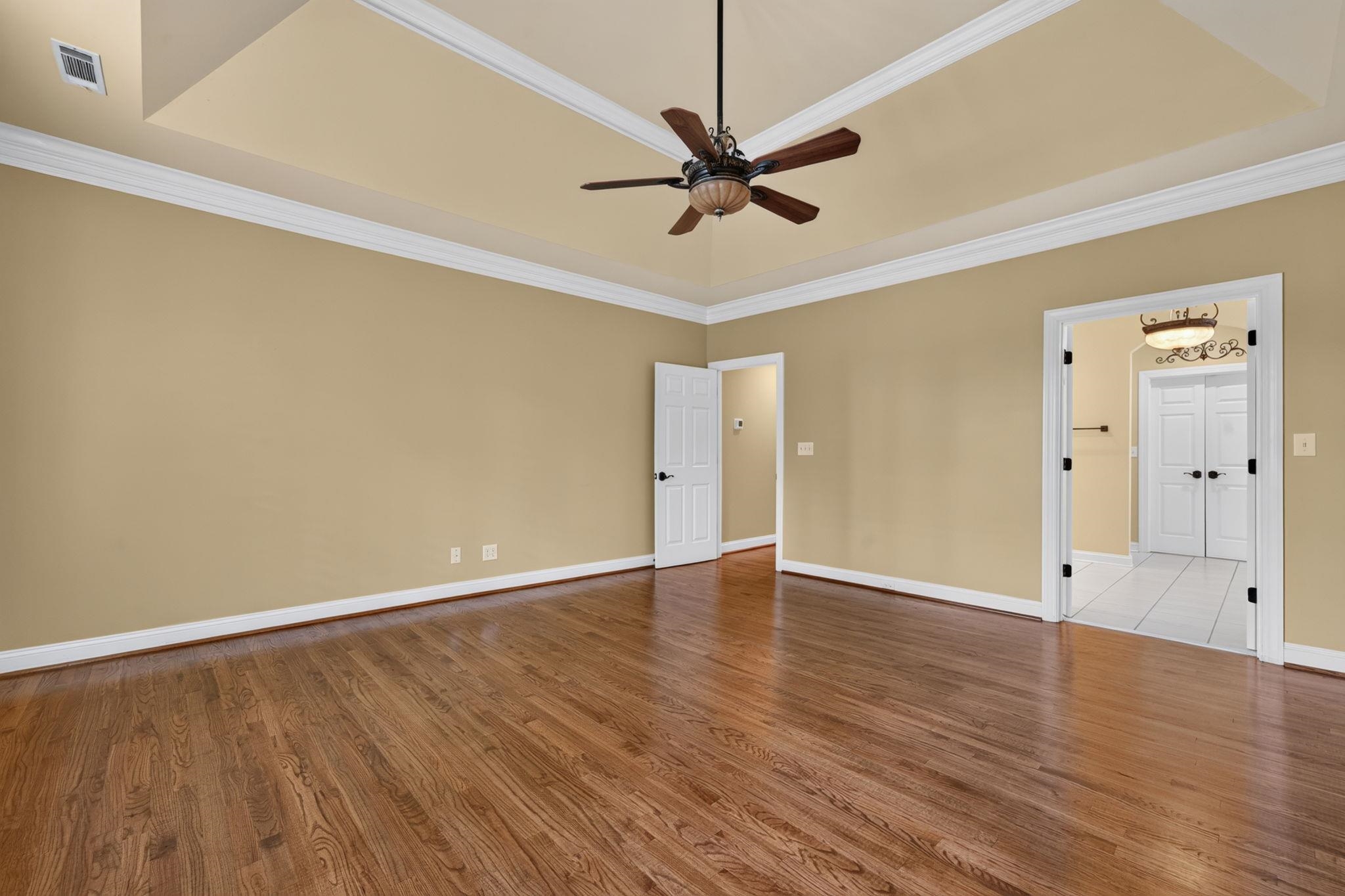Empty room with hardwood floors, a tray ceiling, and open doorways to a tiled bathroom.