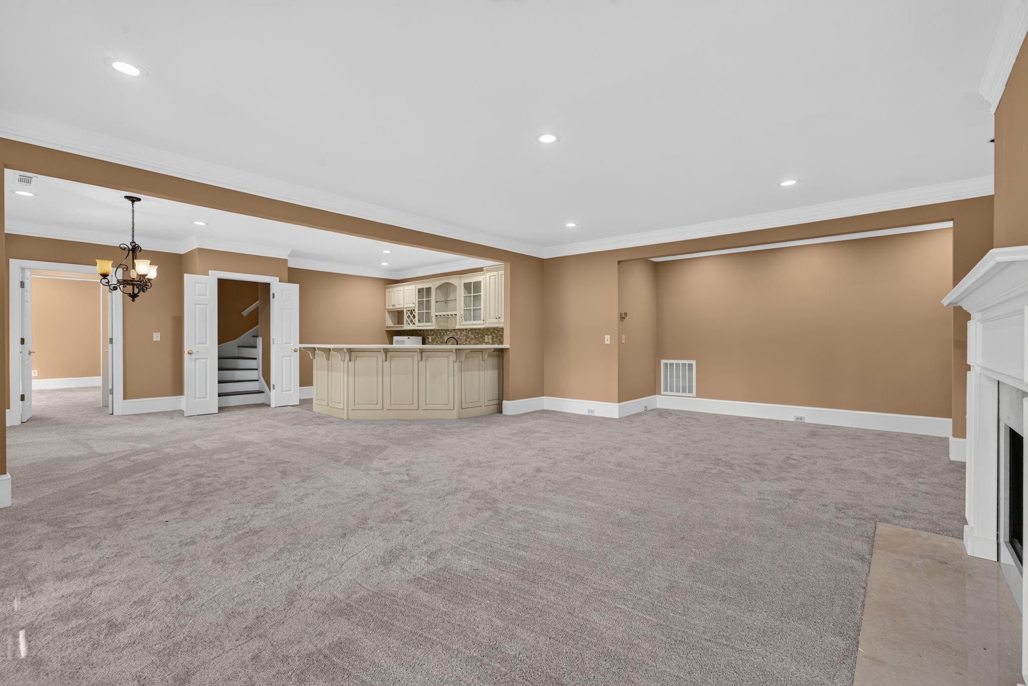 Vacant living room with a built-in wet bar, gray carpet, and white fireplace