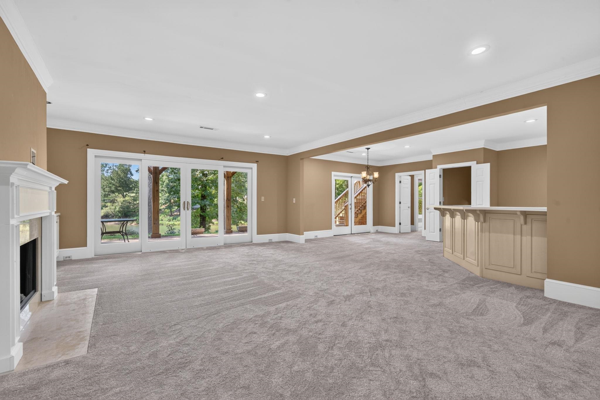 Empty living room with a white fireplace, wide glass doors, and built-in bar.