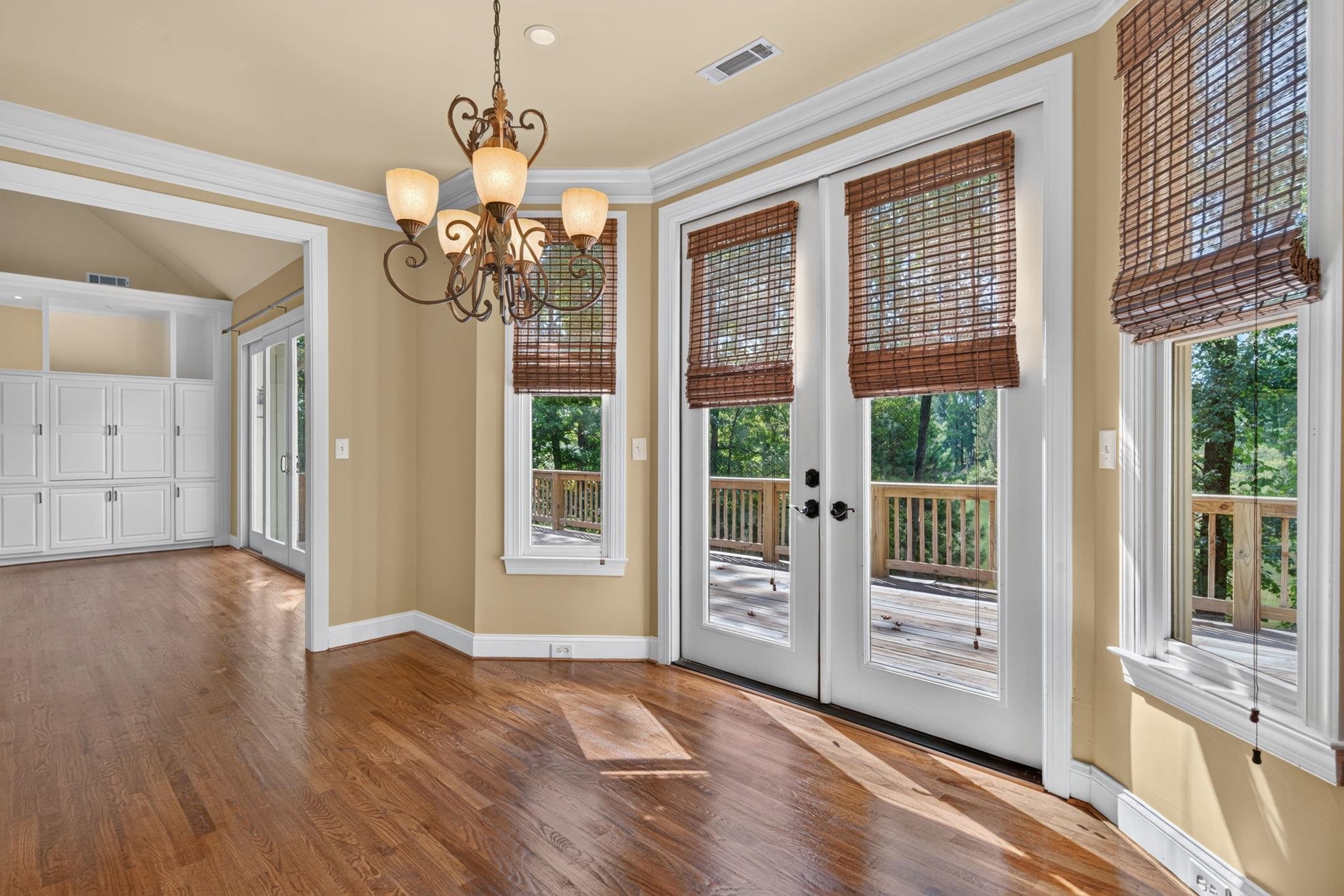 Bright room with hardwood floors, a chandelier, and glass doors opening to a wooded deck.