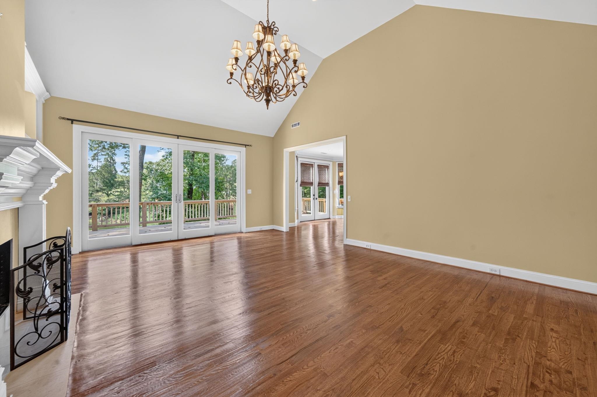 Vacant living room with polished hardwood floors, vaulted ceiling, ornate chandelier, and French doors to a deck.