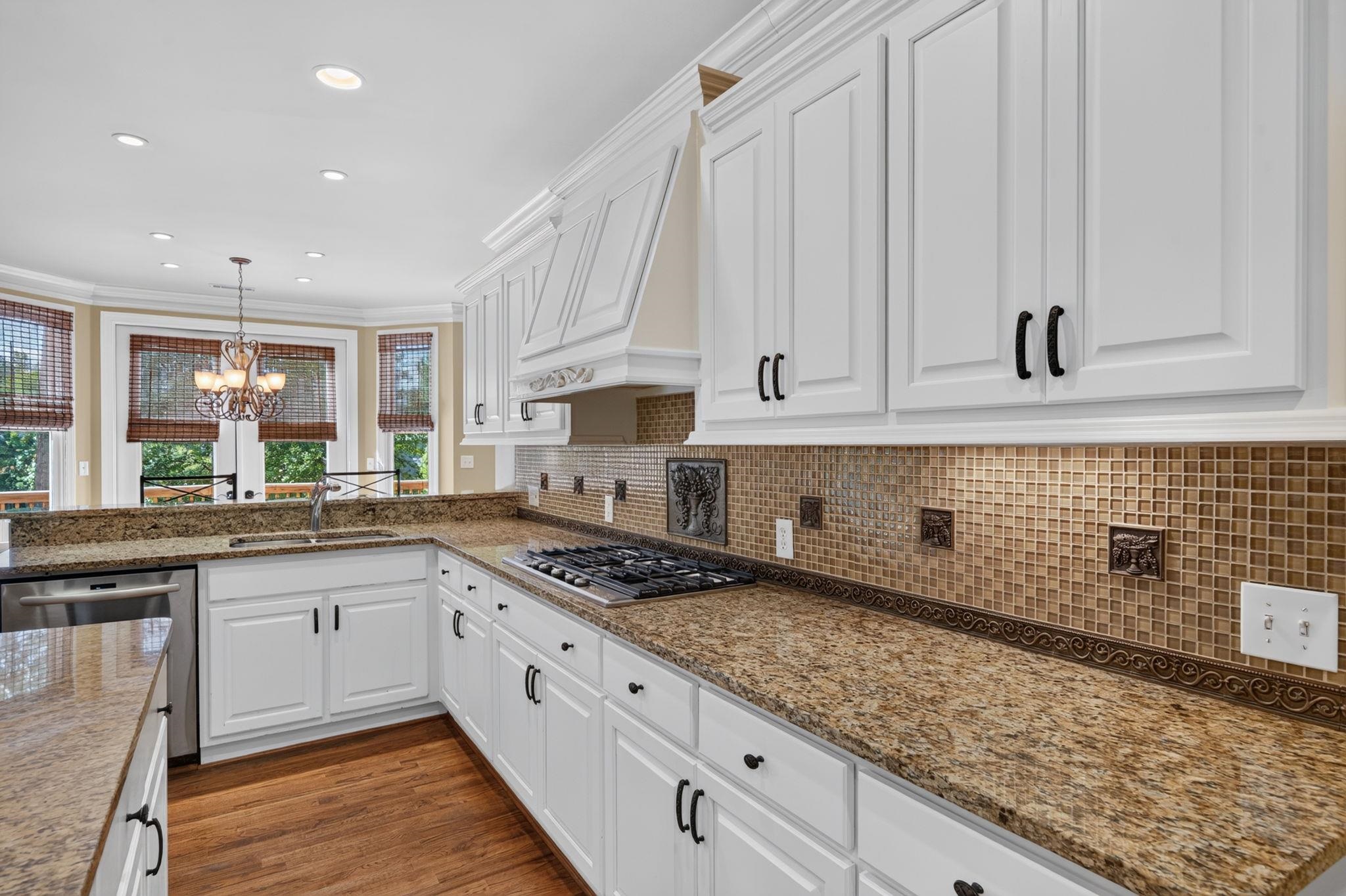 Kitchen with white cabinets, granite counters, tan mosaic backsplash, and a gas cooktop.