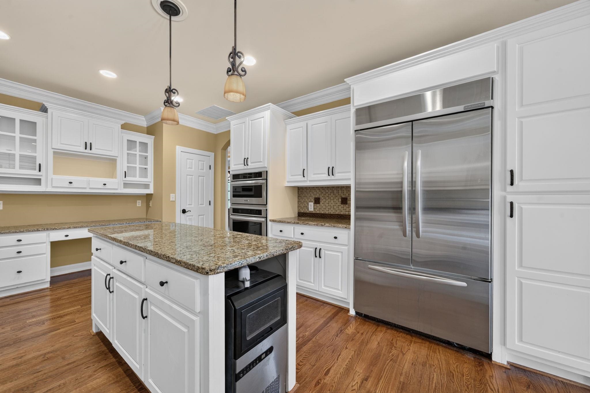 Kitchen with white cabinets, granite island, stainless steel appliances, and hardwood floors.