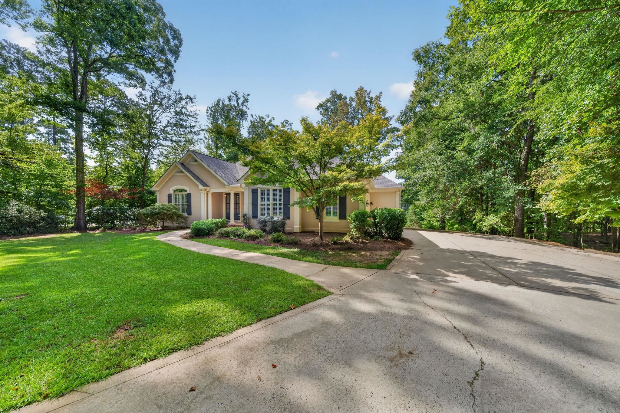Beige home framed by mature trees, with a broad driveway and green lawn.