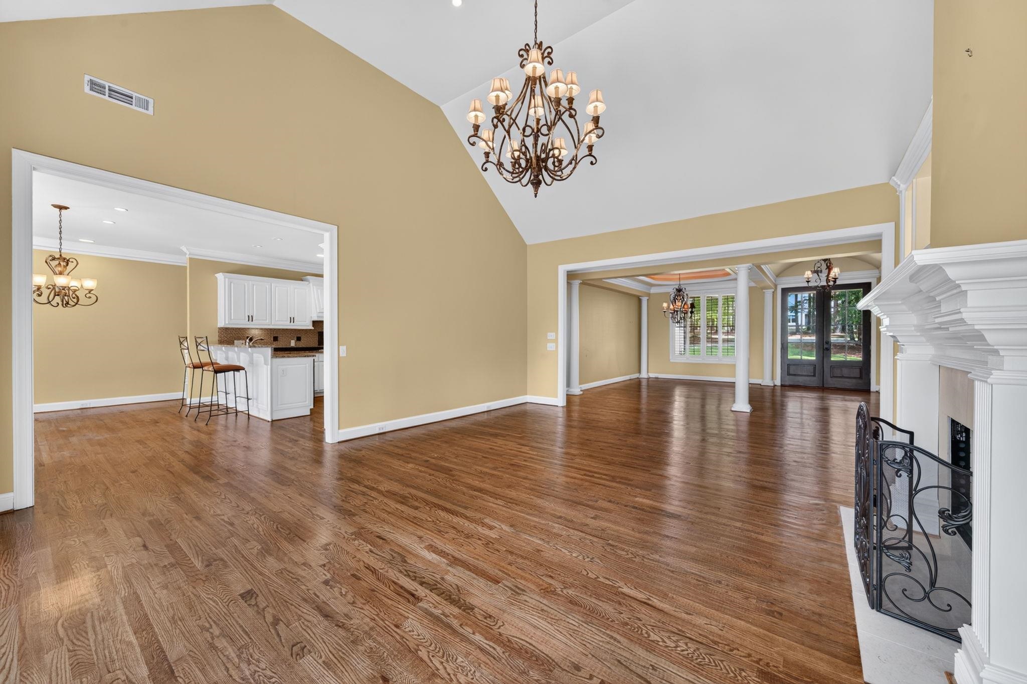 Living room with vaulted ceiling, hardwood floors, white fireplace, and a view into the dining area.