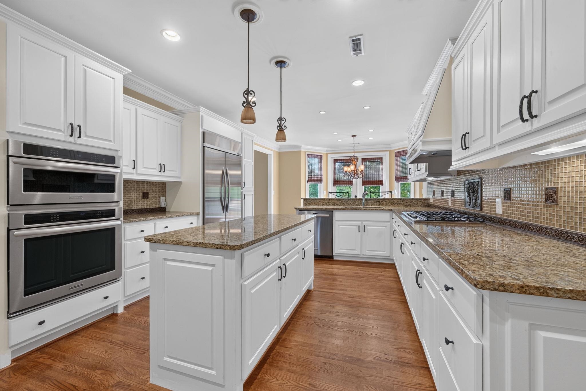 Kitchen with a large granite island, white cabinetry, stainless steel appliances, and hardwood floors.