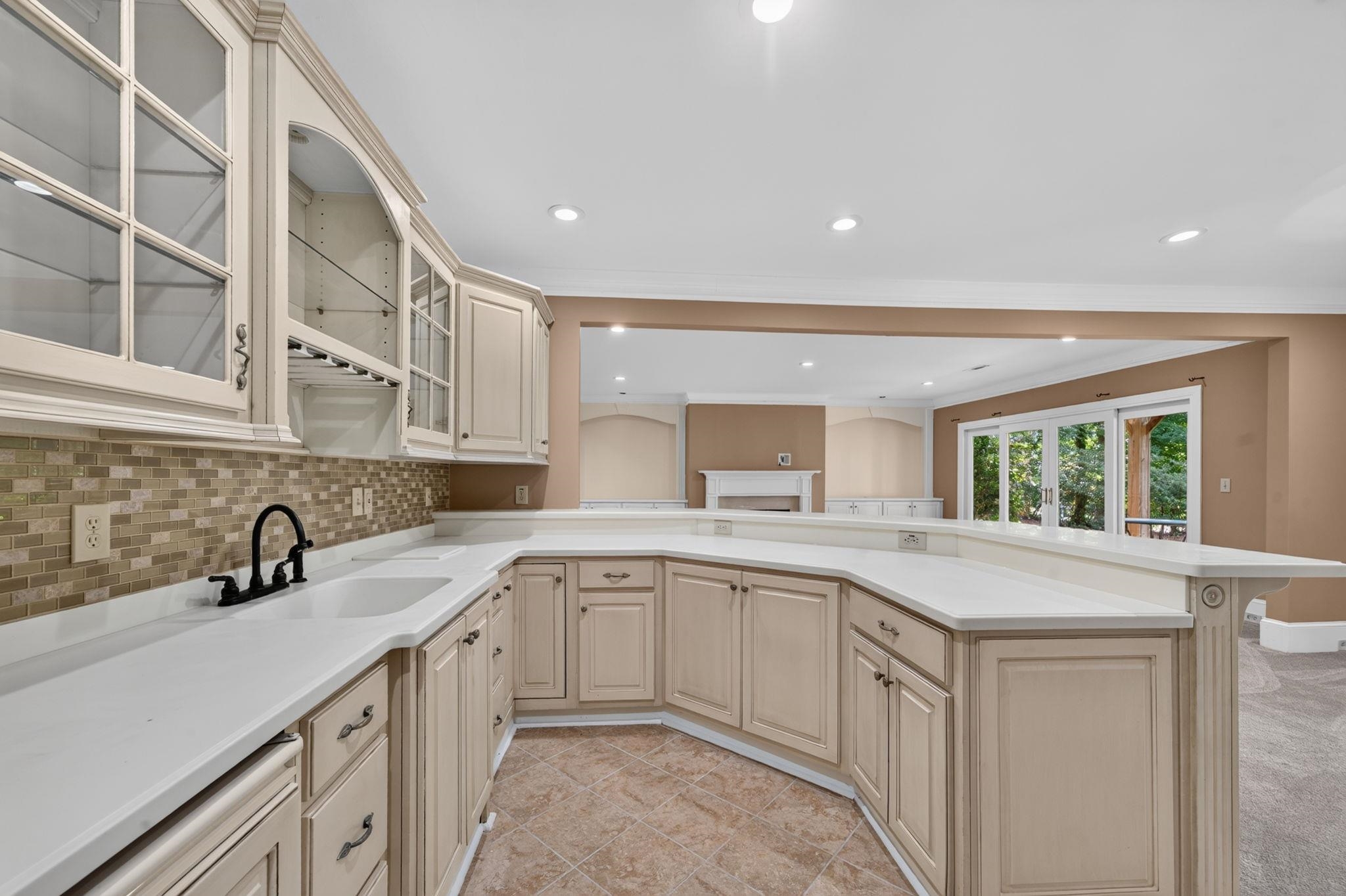 Kitchen with cream cabinets, white counters, mosaic tile backsplash, and an open view into the living area.