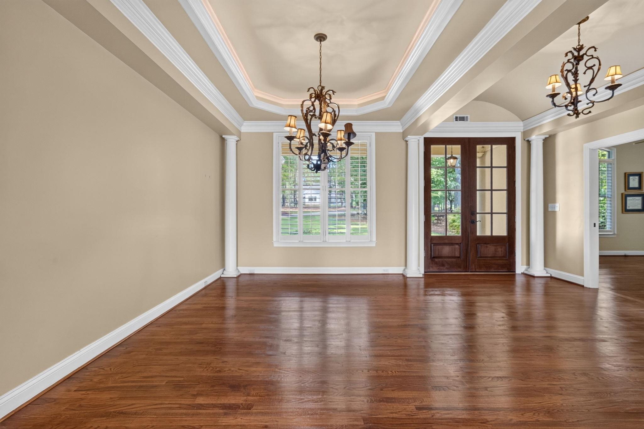 Empty dining room with hardwood floors, tray ceiling, chandeliers, and French doors.
