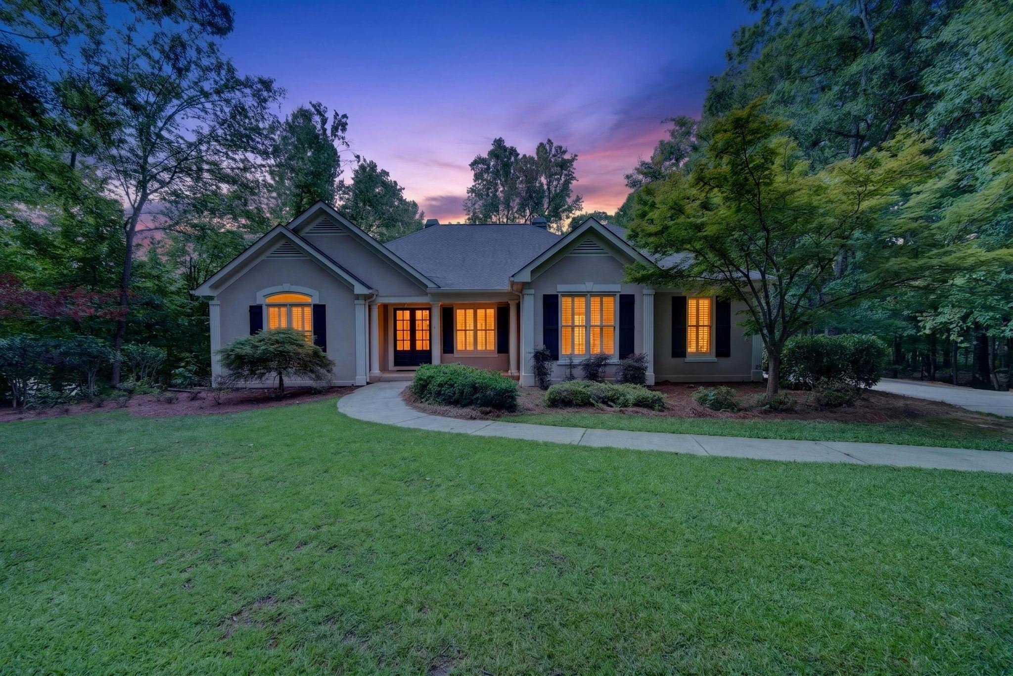 Single-story home at dusk with glowing windows, a curved walkway, and a broad lawn.