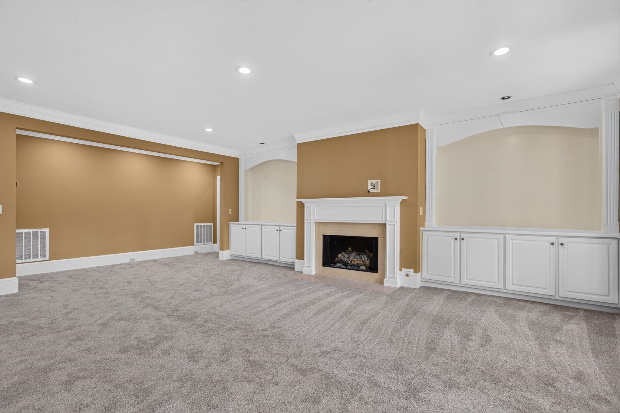 Empty living room with a white fireplace, built-in cabinets, and gray carpet.