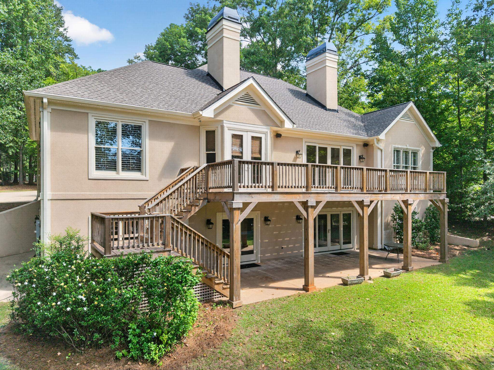 Home’s rear exterior with a large wooden deck, stairs, and covered patio beneath.