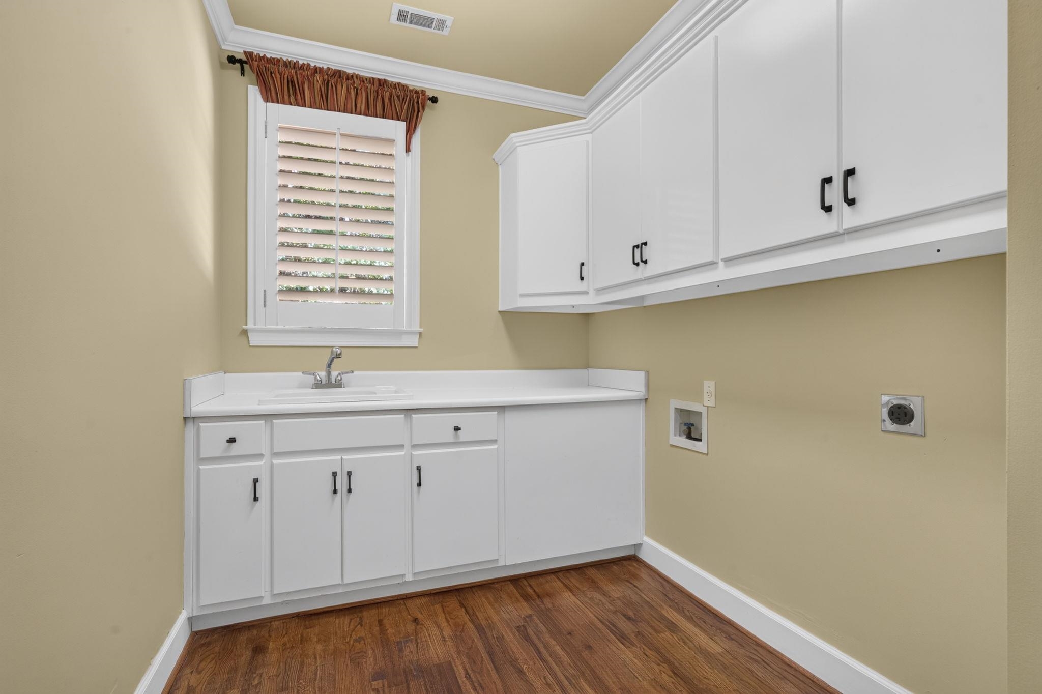 Laundry room with white cabinets, utility sink, washer and dryer hookups, and hardwood floors.