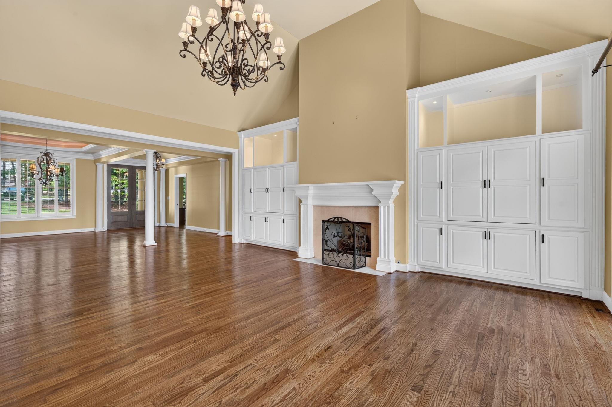 Empty living room with hardwood floors, a white fireplace, and built-in cabinets.