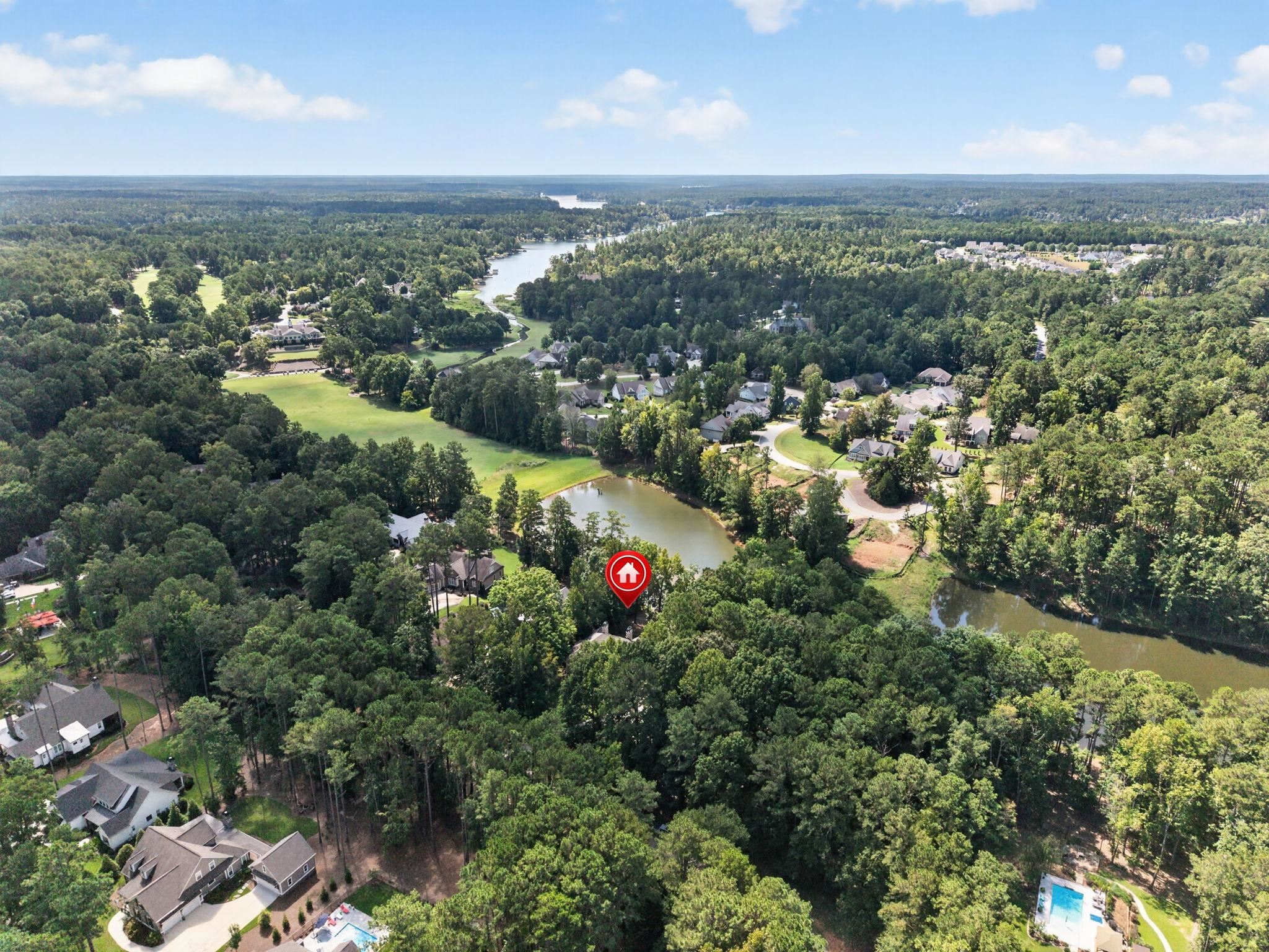 Aerial view of a wooded neighborhood with ponds and a red marker for the property.