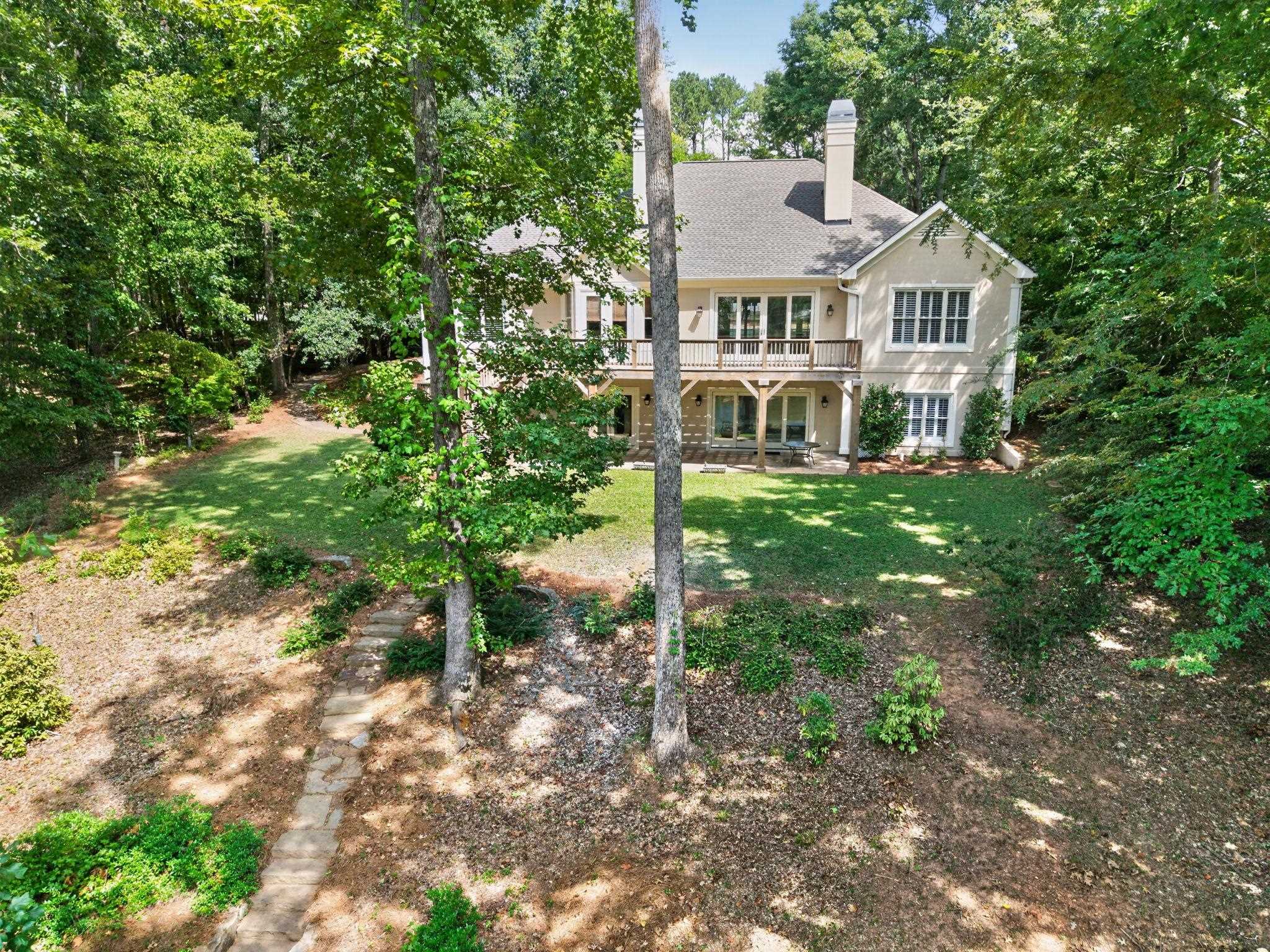 Rear of a beige two-story home with an upper deck, covered patio, and wooded yard.