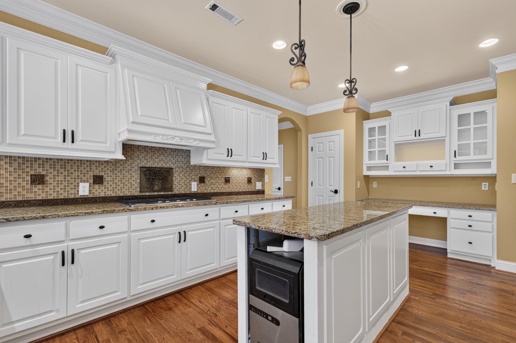 Kitchen with white cabinetry, a granite island, mosaic tile backsplash, and hardwood floors.
