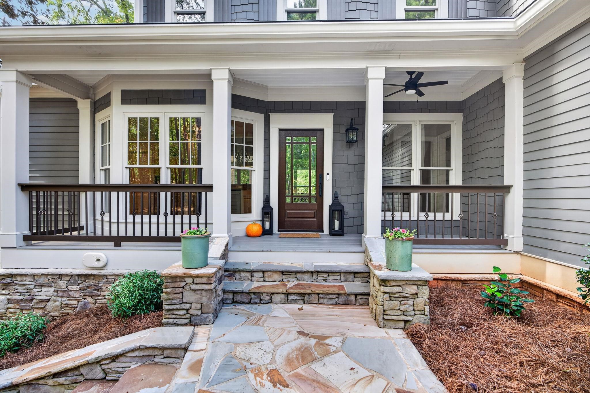 Home’s covered front porch with a glass-paneled wood door, white columns, and stone entry steps.