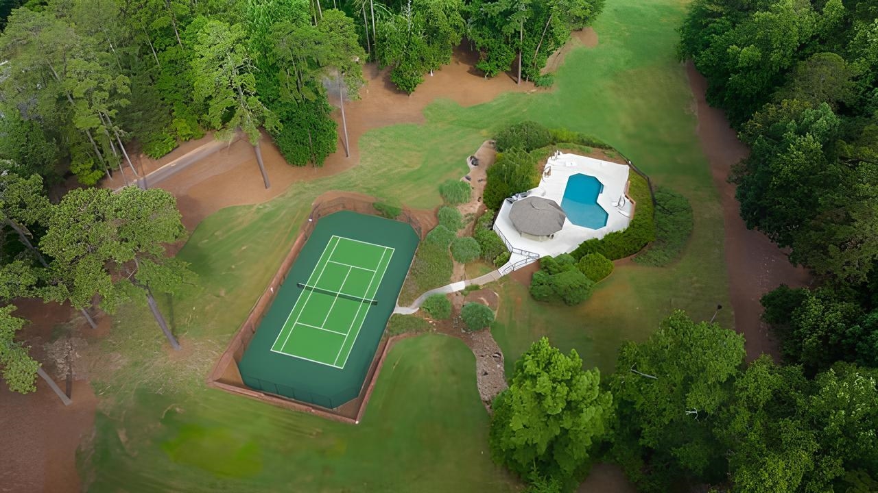 Aerial view of a landscaped property with a tennis court and pool among mature trees.