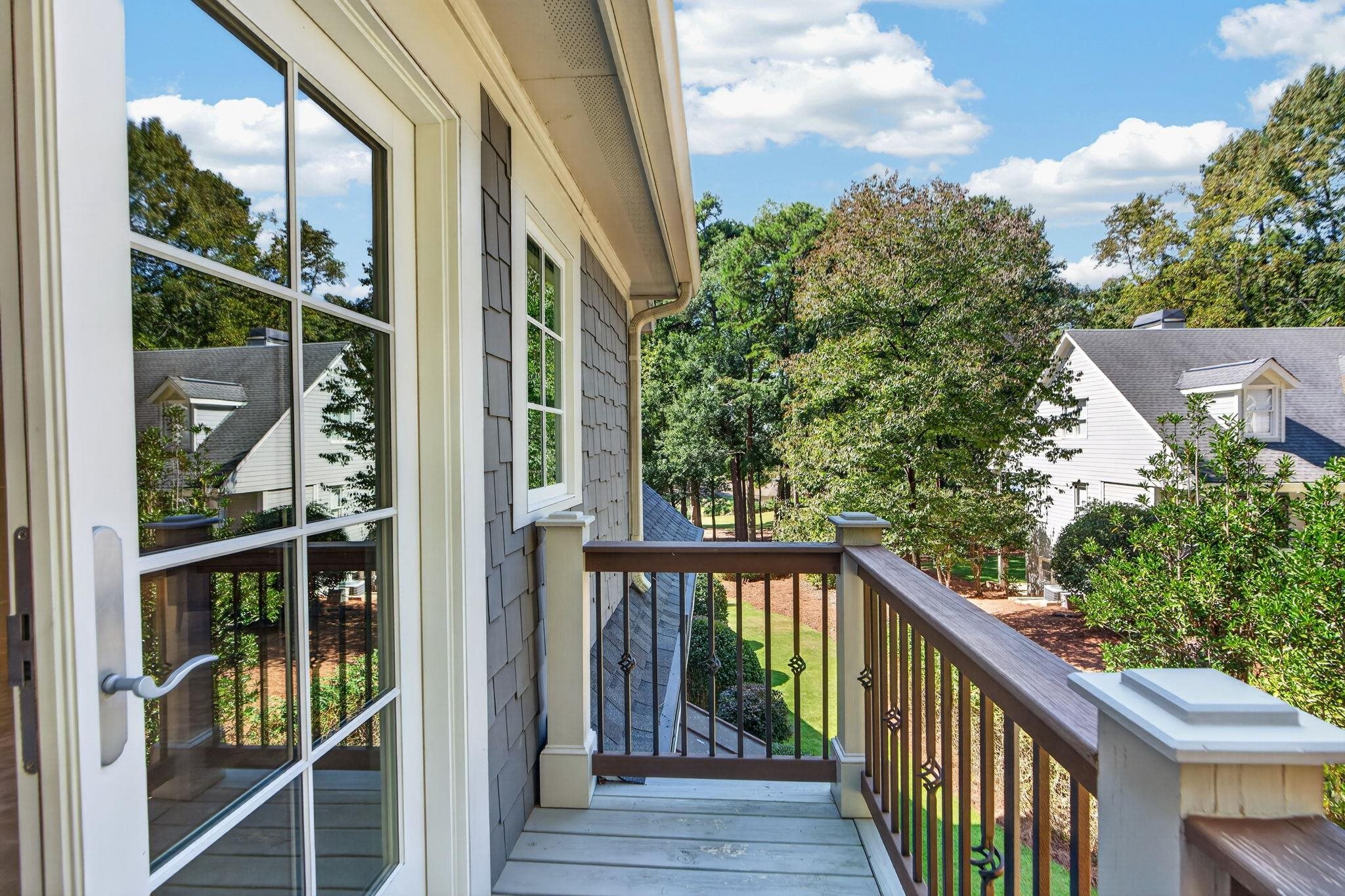 Second-story balcony with dark railings overlooking trees, lawn, and neighboring homes.