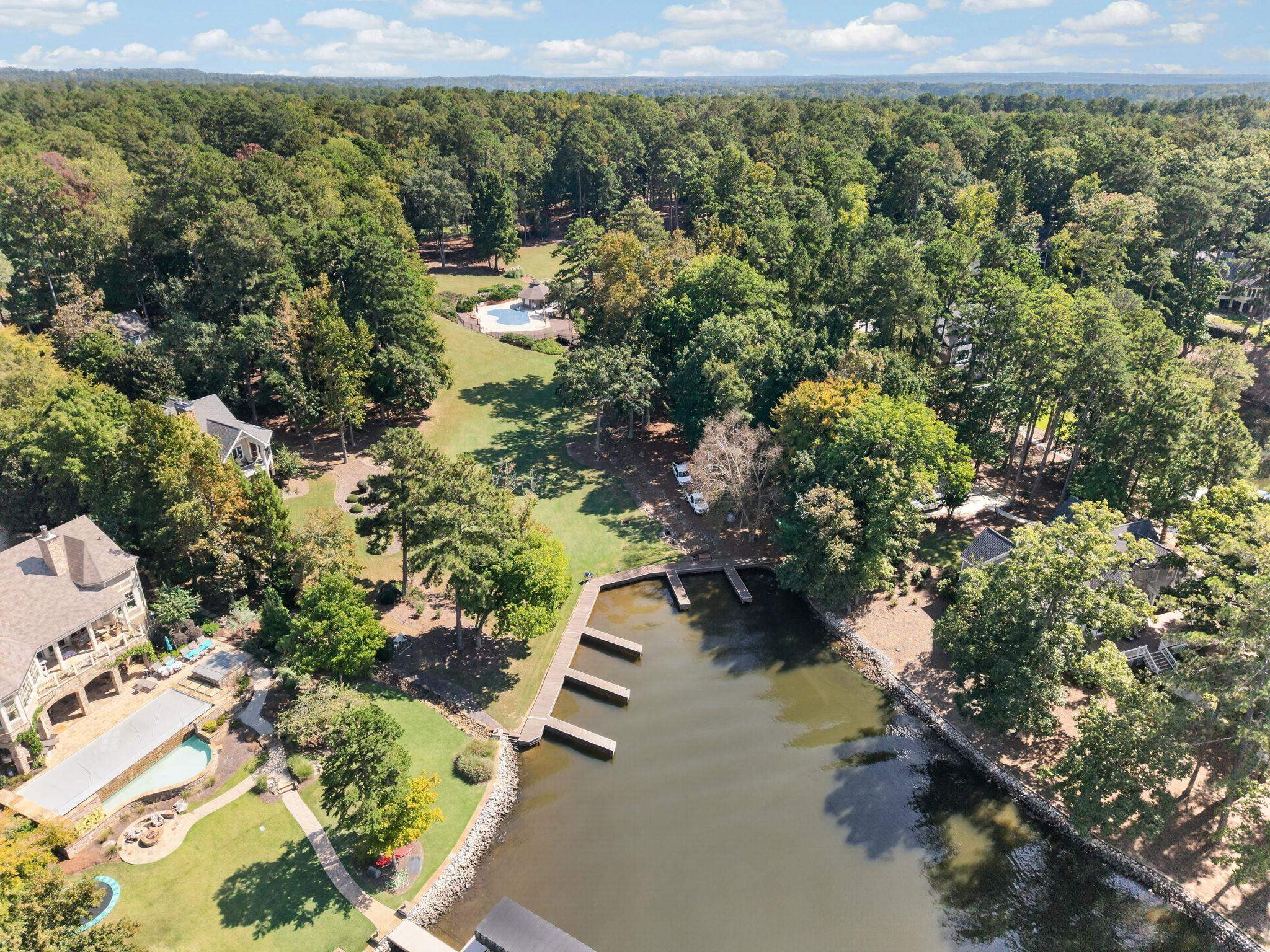 Aerial view of a wooded waterfront home with a swimming pool and dock.
