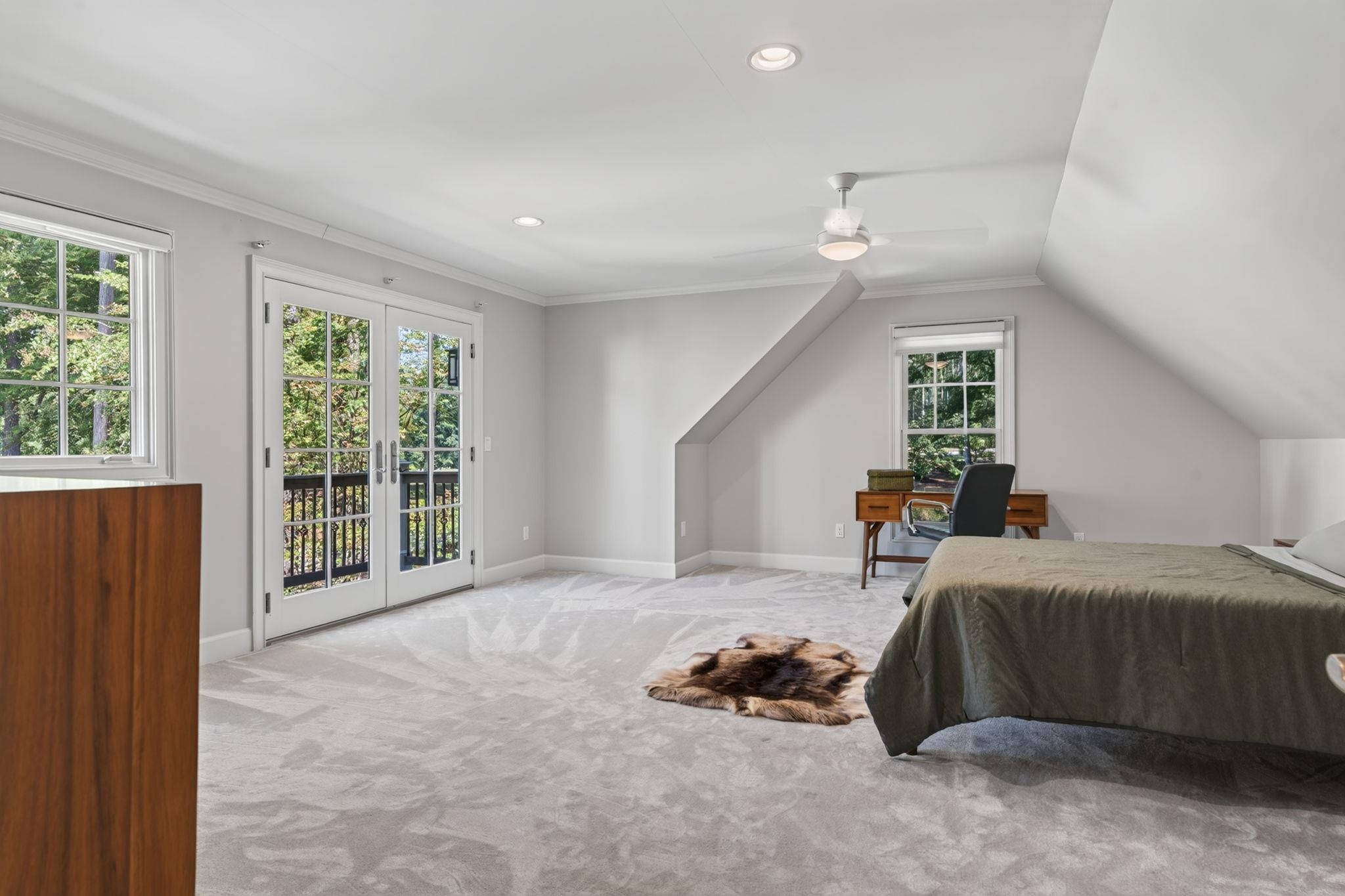 Attic bedroom with a sloped ceiling, French doors to a balcony, and a desk beside the bed.