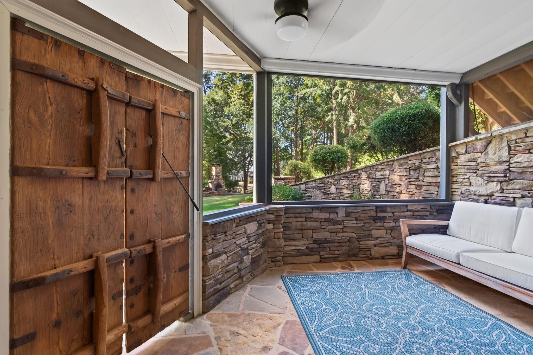 Enclosed porch with a rustic wooden door, stone walls, large windows, and a white sofa.
