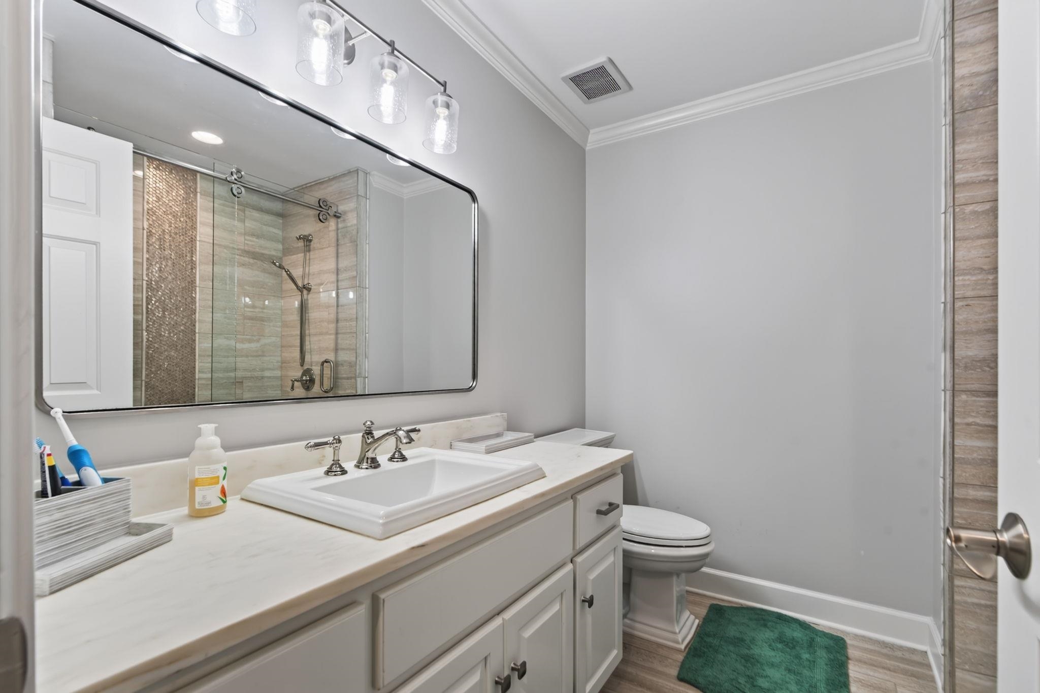 Bathroom vanity with a large mirror, glass shower, and green bath mat.