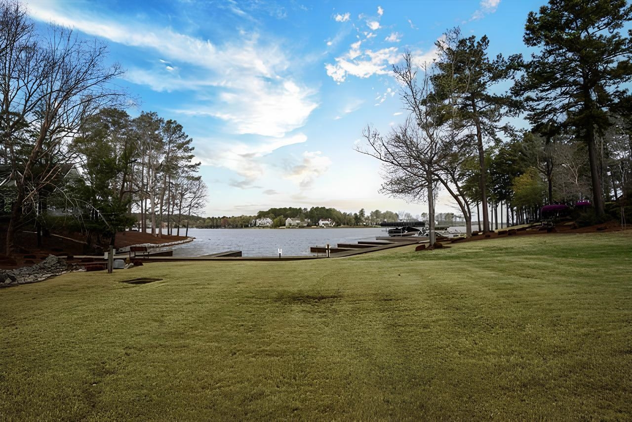 Grassy lawn slopes toward a lake with docks and boats along the tree-lined shore.
