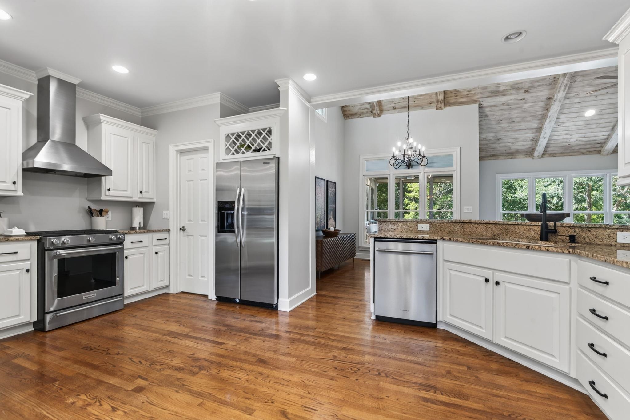 Kitchen with white cabinets, stainless steel appliances, granite counters, and a vaulted wood-beam ceiling.