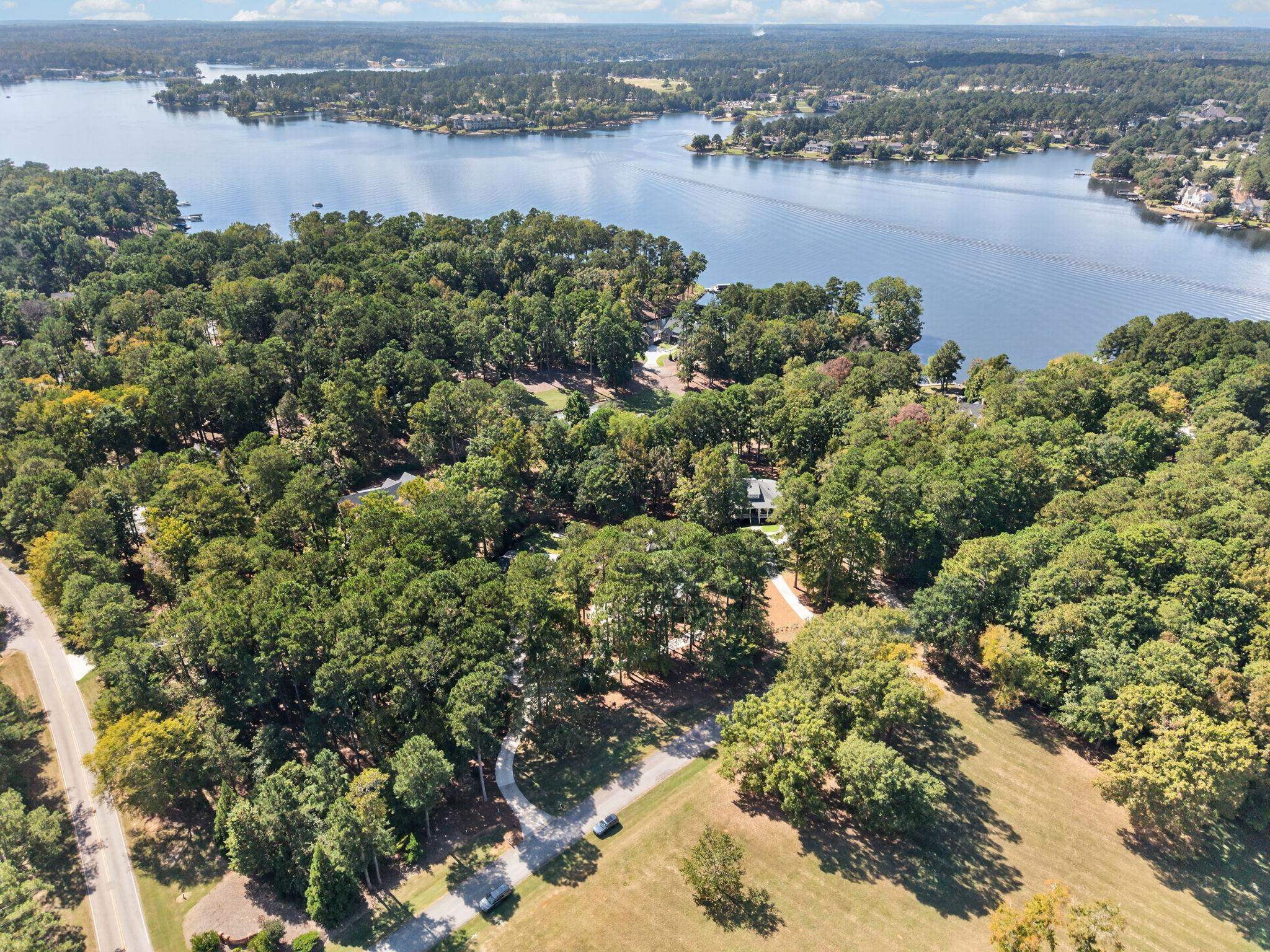 Aerial view of wooded homes beside a broad lake, with neighborhood roads in the foreground.