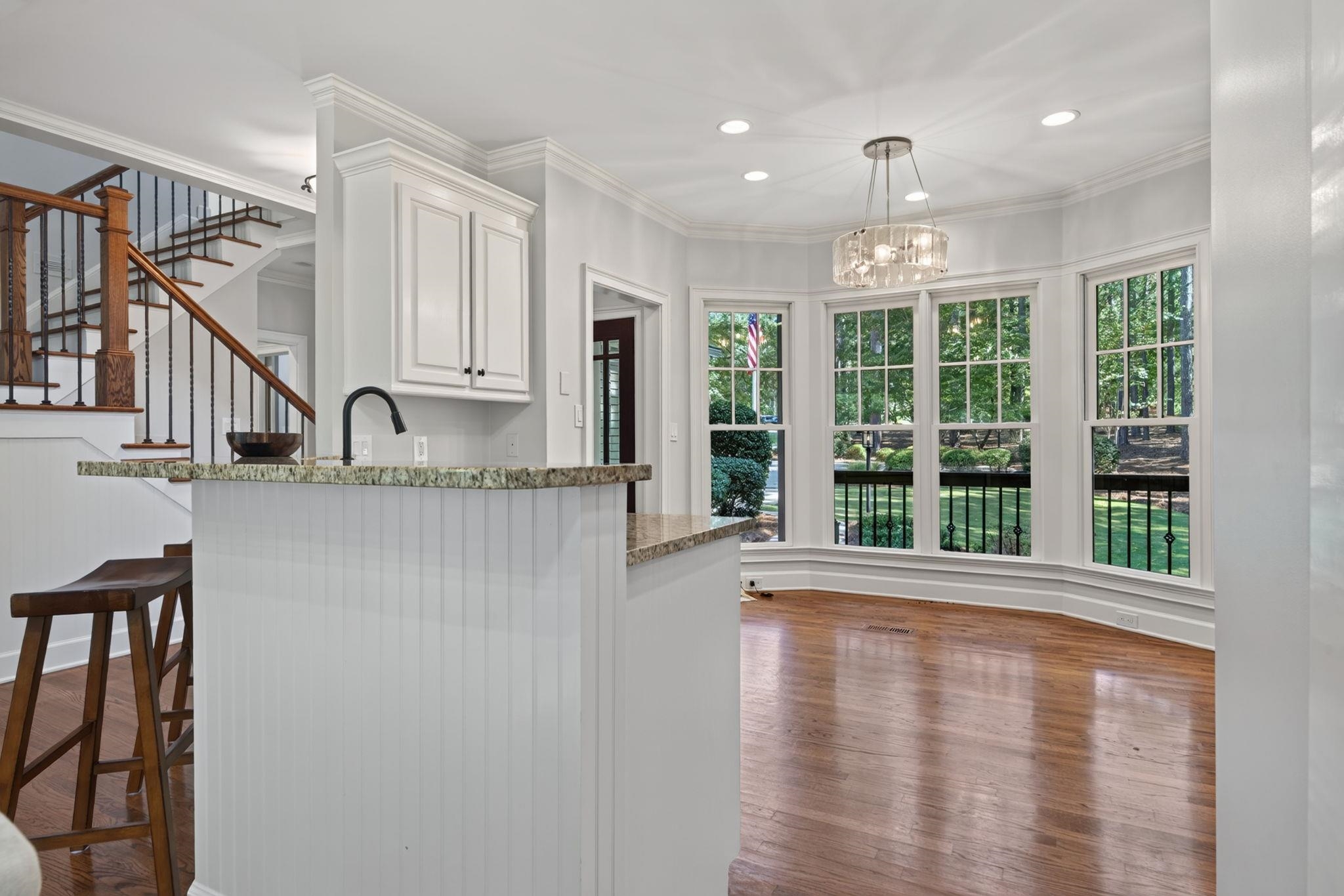 Dining area with hardwood floors, a crystal chandelier, and tall windows overlooking trees.