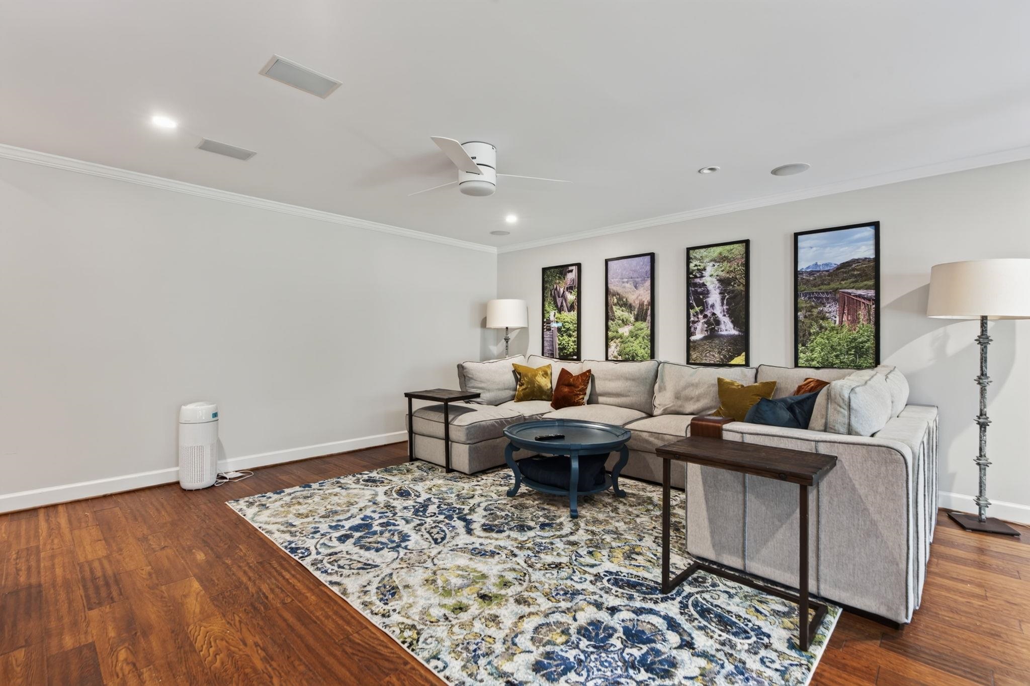 Living room with a light sectional, patterned rug, hardwood floors, and framed landscape photographs.