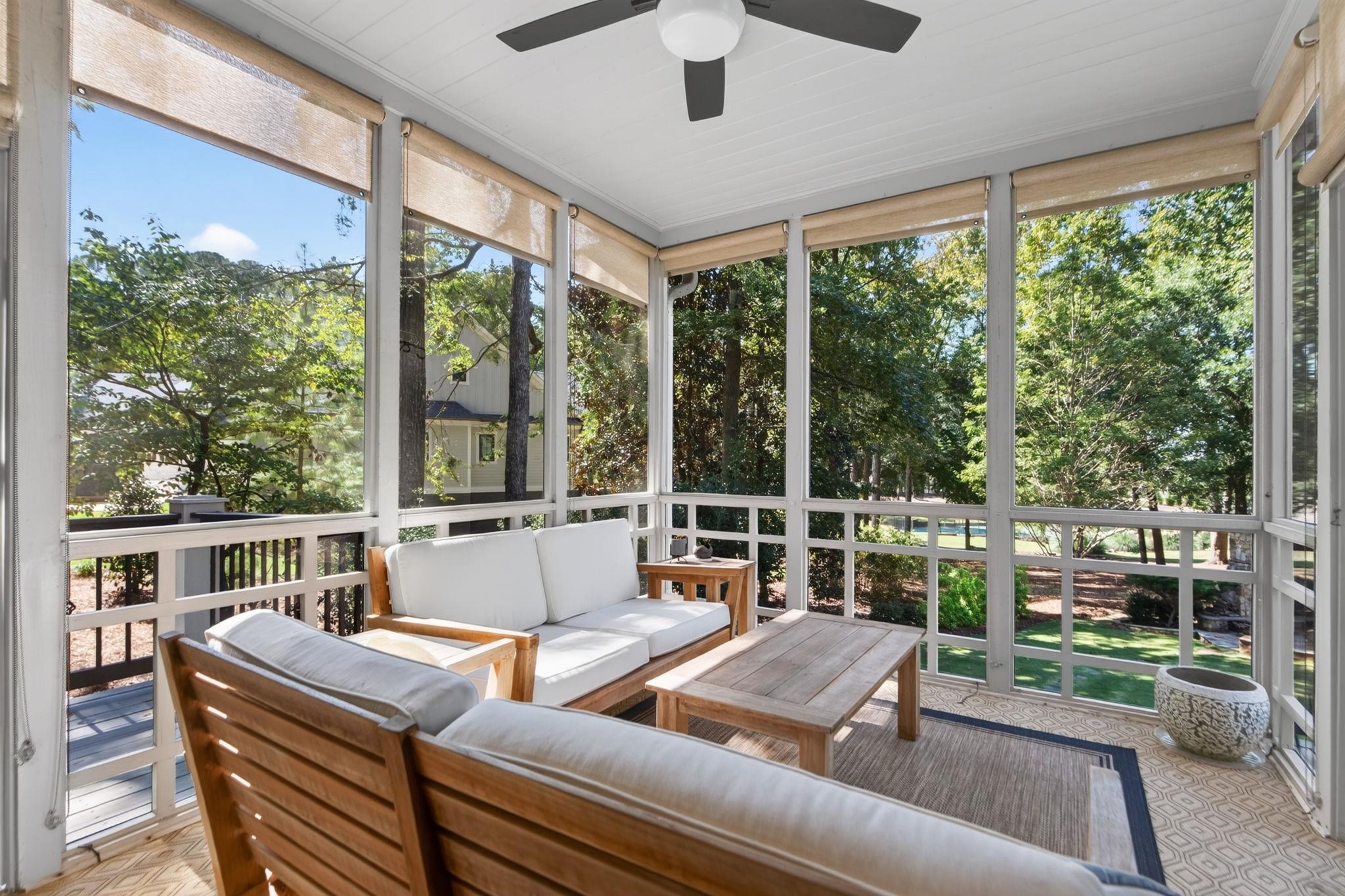 Screened porch with cushioned wooden seating and views of a leafy yard.