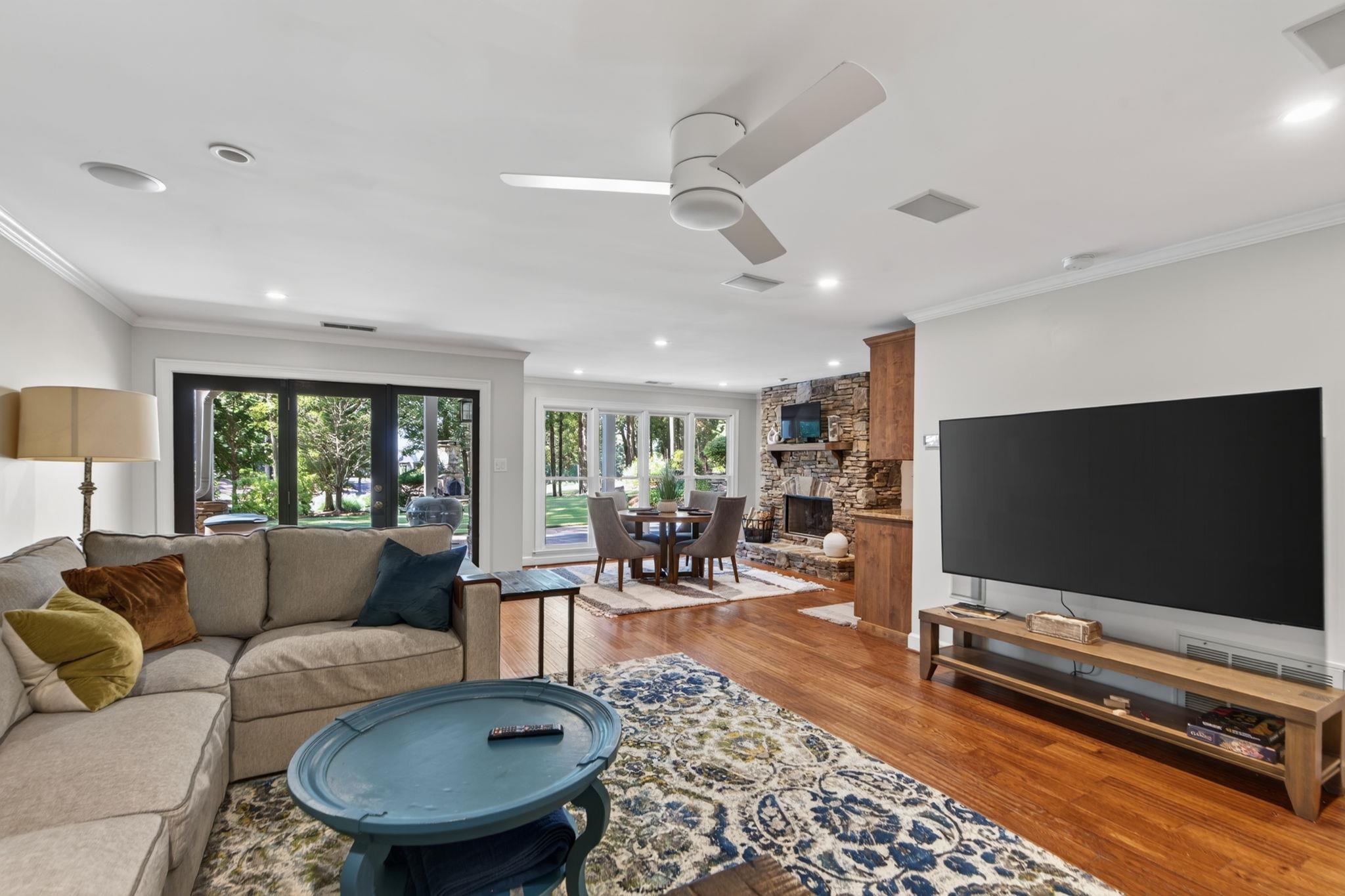 Living room with a stone fireplace, hardwood floors, and glass doors opening toward leafy trees.