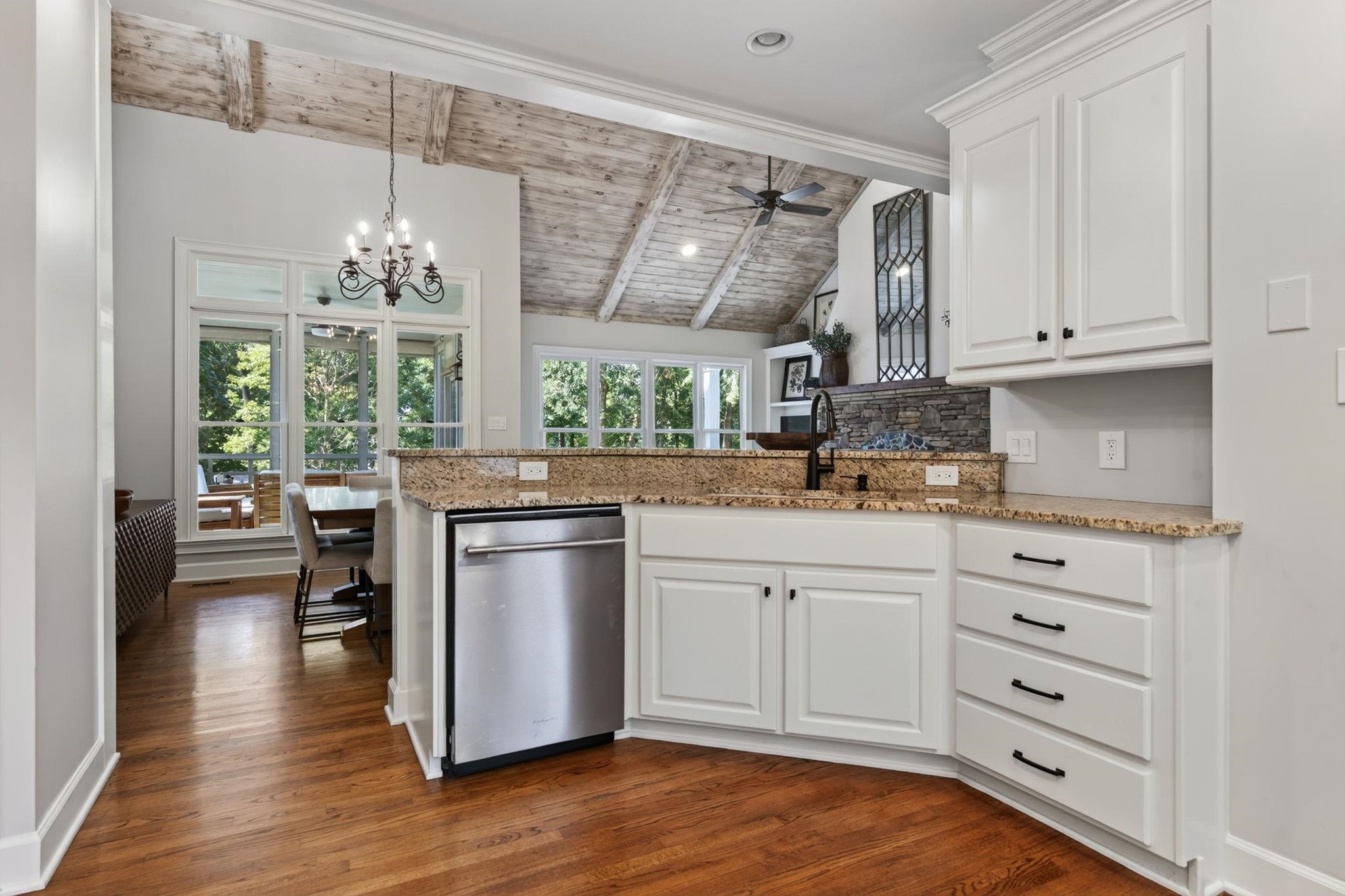Bright kitchen with vaulted wood ceiling, granite counters, white cabinetry, and stainless steel dishwasher.
