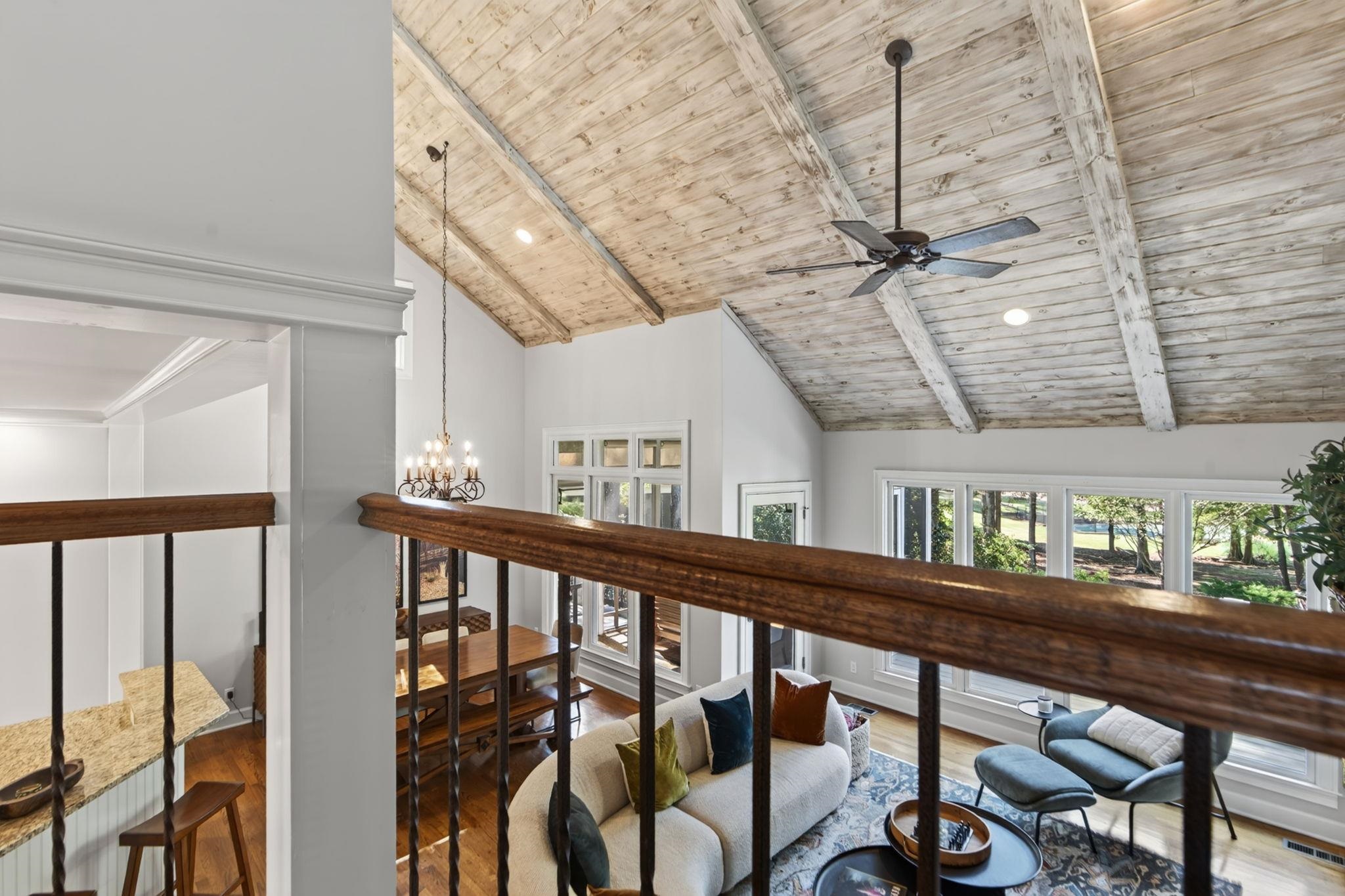 Living room with vaulted wood ceiling, dark railing, and large windows overlooking the seating area.