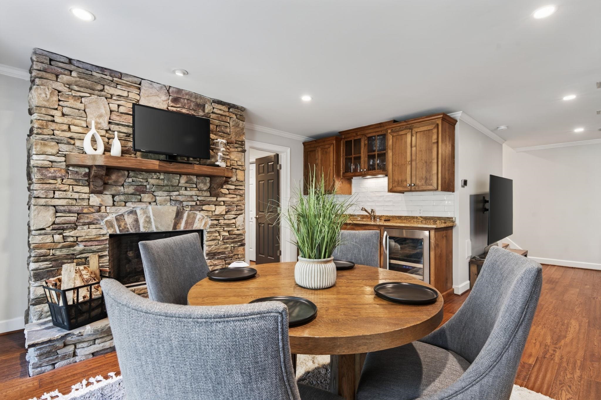 Dining area with a round wooden table beside a stacked-stone fireplace and built-in cabinetry.
