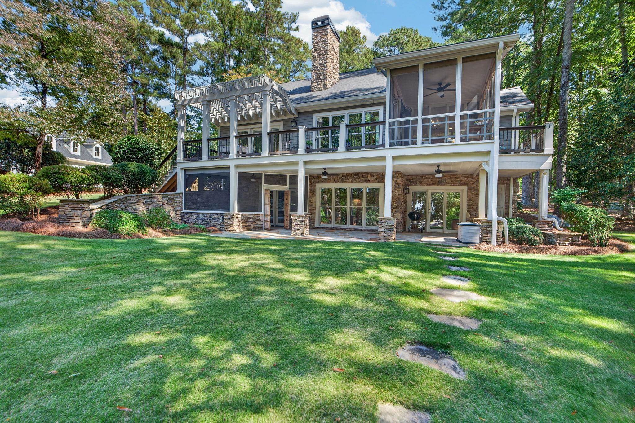 Rear of a two-level home with a screened porch, stone lower level, deck, and expansive lawn.