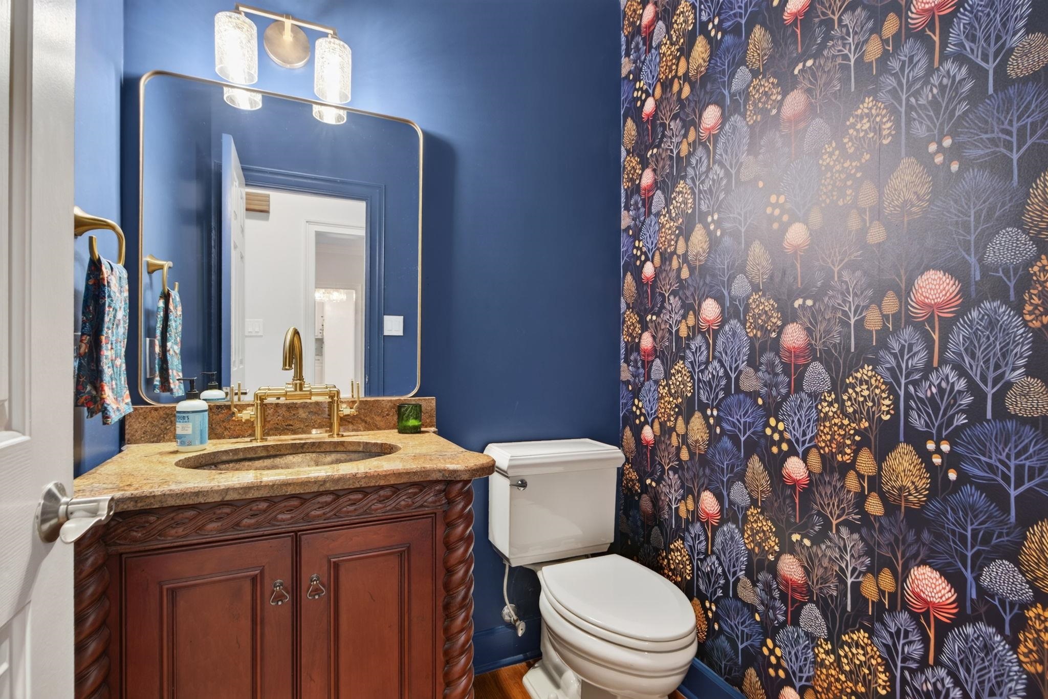 Powder room with botanical wallpaper, navy walls, and a carved wood vanity with a gold faucet.