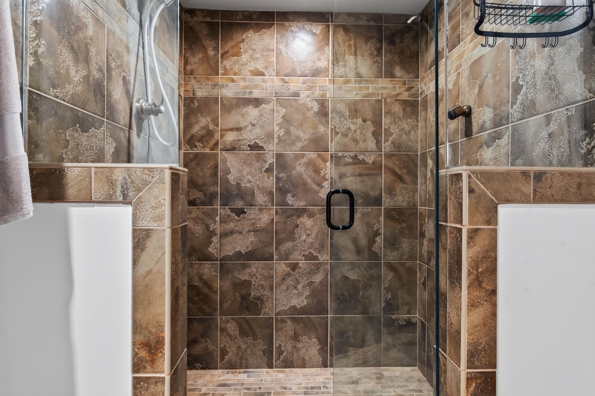 Tiled bathroom shower with glass door and black handle.