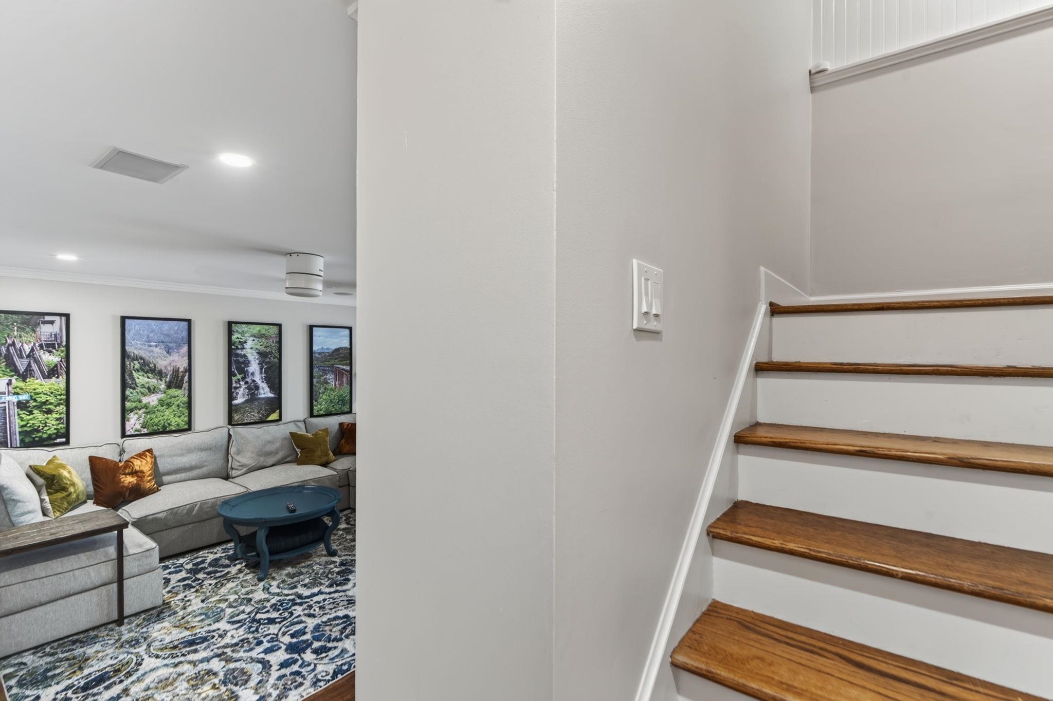 Wood-tread staircase beside a living room with a gray sectional and patterned rug.