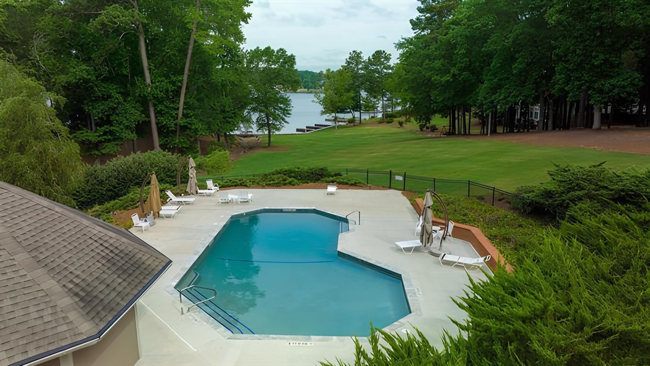 Outdoor pool and lounge deck overlooking a tree-lined lawn and lake.
