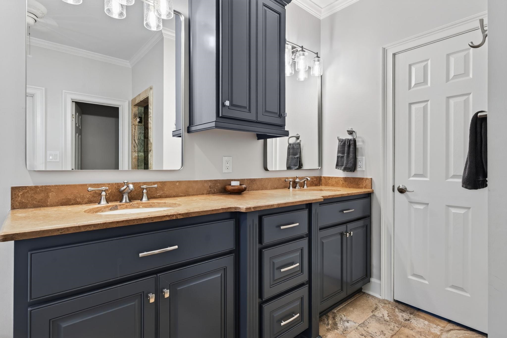 Bathroom double vanity with dark cabinetry, tan stone counters, and large mirrors.