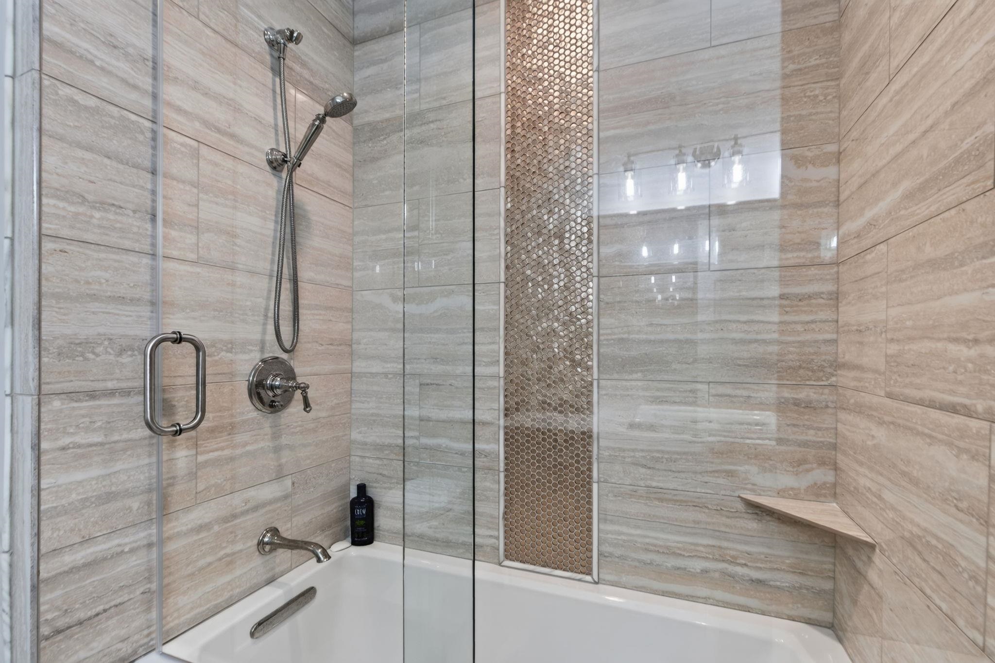 Bathroom tub and glass-enclosed shower with beige tile and a narrow mosaic accent strip.