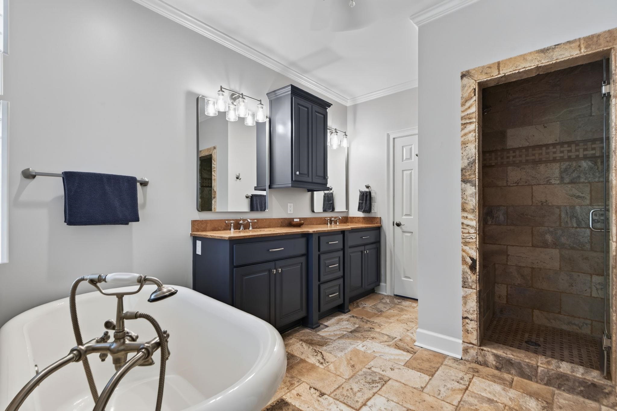 Bathroom with a freestanding tub, dark double vanity, and stone-framed walk-in shower.