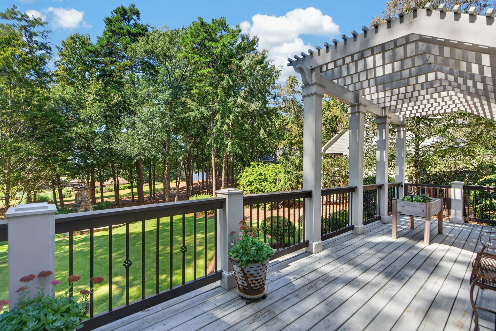 Wooden deck with a white pergola overlooks a tree-lined lawn and a glimpse of water.