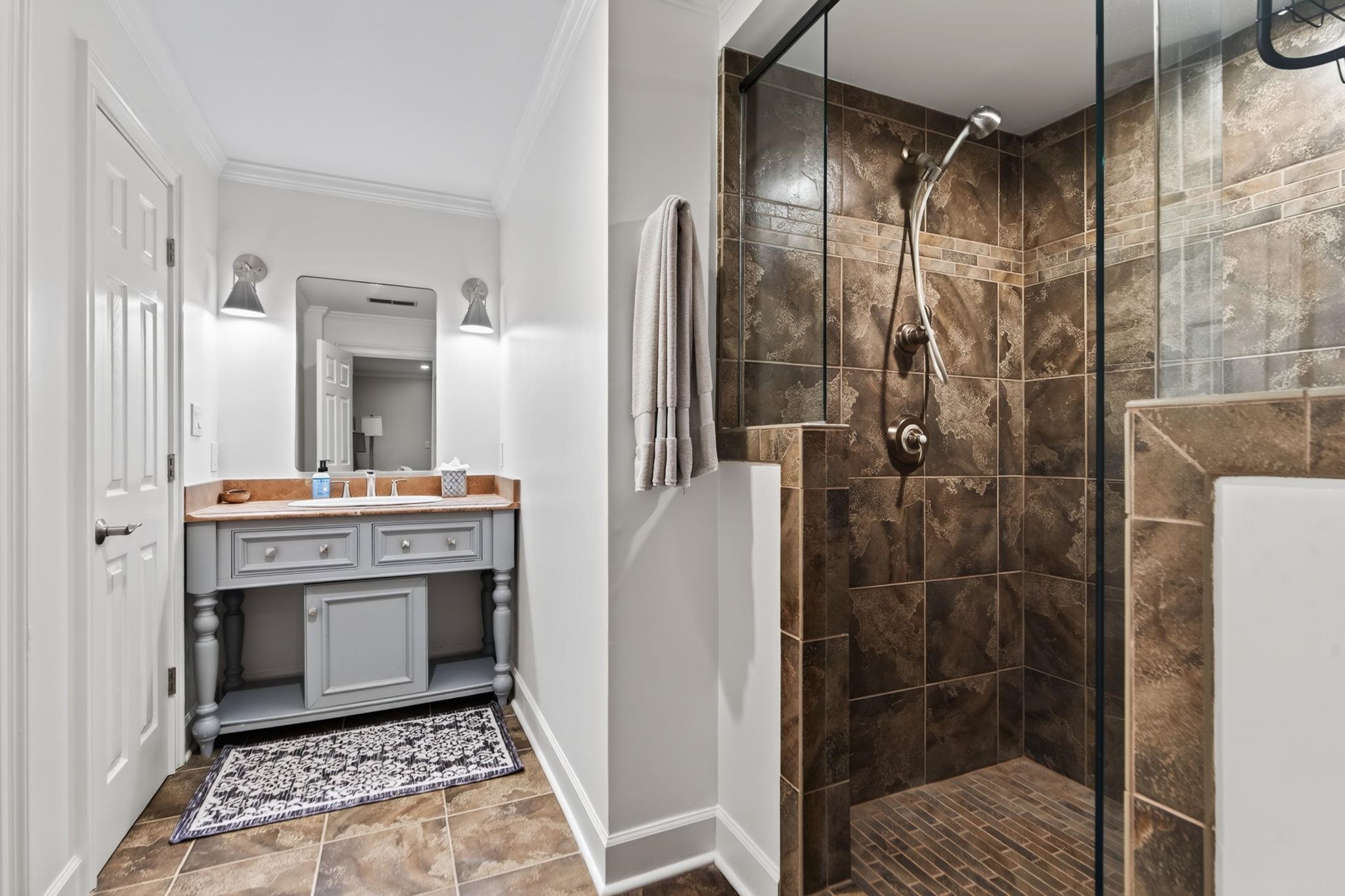Bathroom with a gray vanity and a glass-enclosed brown-tile walk-in shower.