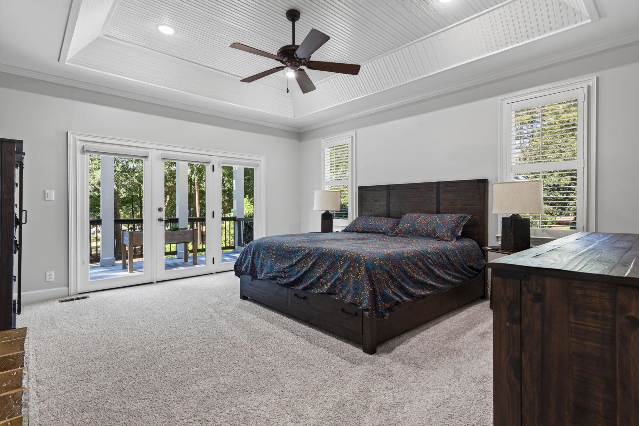 Bedroom with a dark wood bed, tray ceiling, and glass doors opening onto a wooded deck.