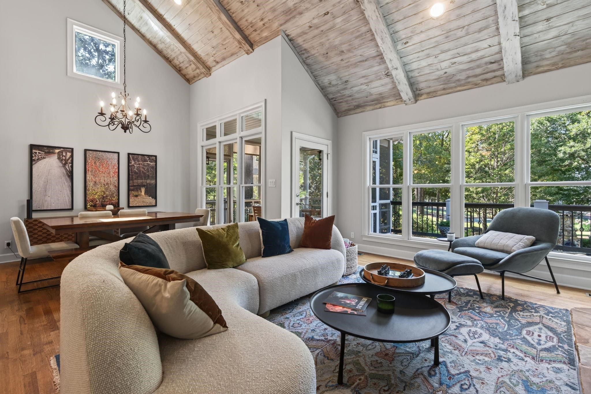 Living room with a curved cream sectional, vaulted wood ceiling, and large windows overlooking trees.